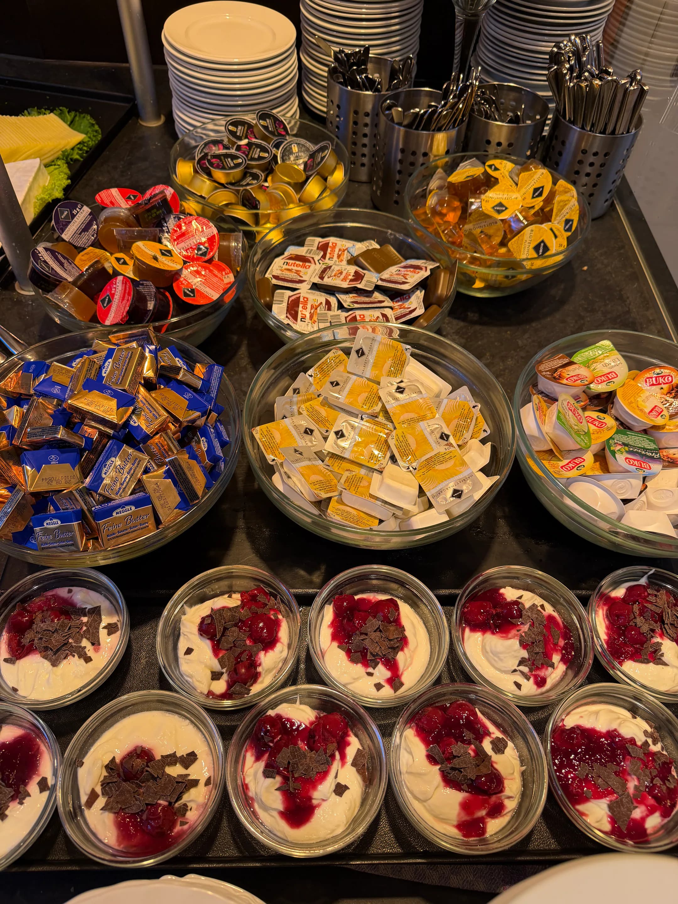 Frühstücksbuffet mit Portionspackungen und kleinen Joghurtgläsern mit roter Fruchtsoße und Schokolade