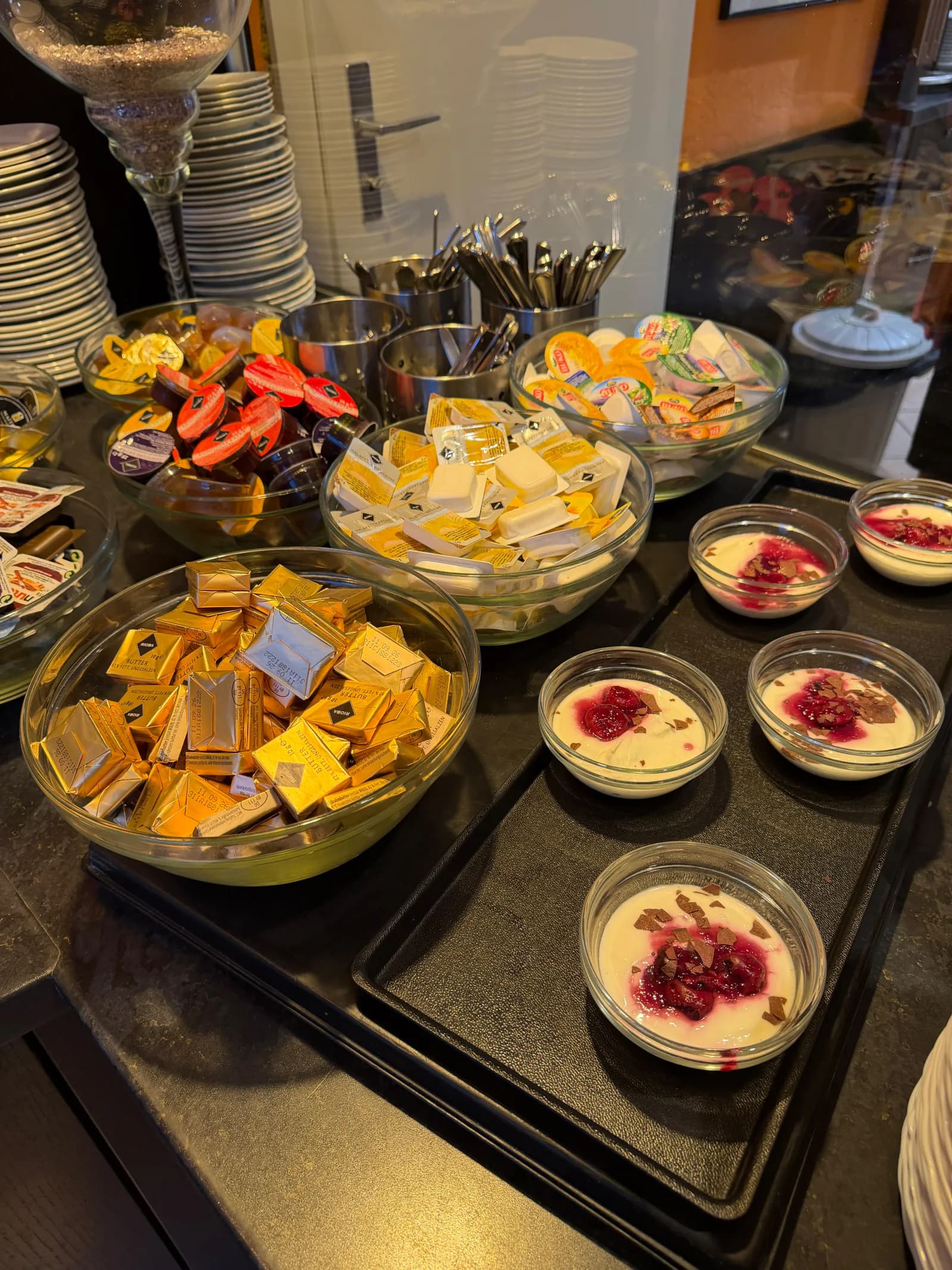 Portionspackungen mit Butter und Aufstrichen neben Dessertgläsern mit roter Fruchtsoße