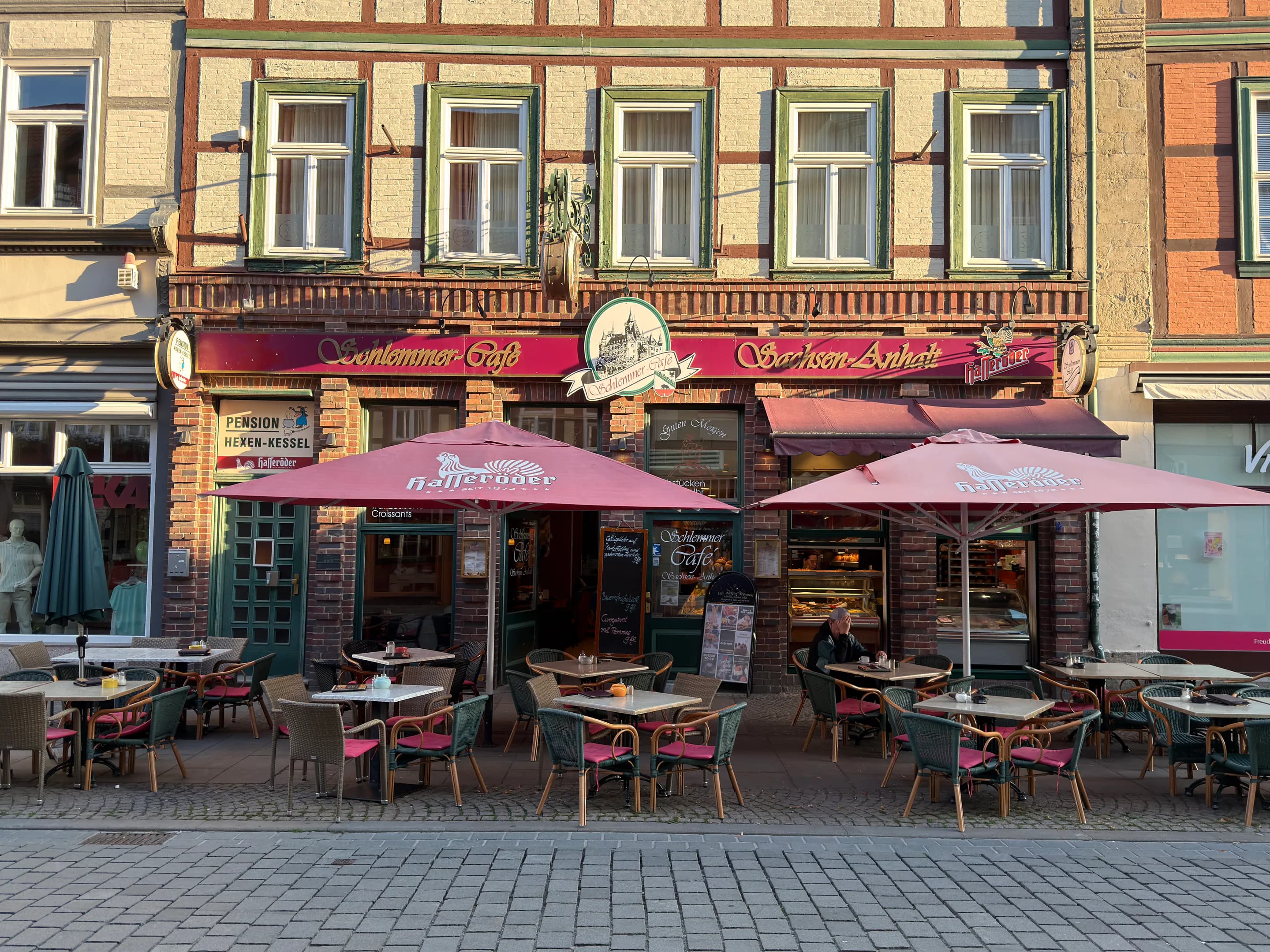 Frontale Außenansicht des Schlemmercafés mit Tischen, Stühlen und roten Sonnenschirmen