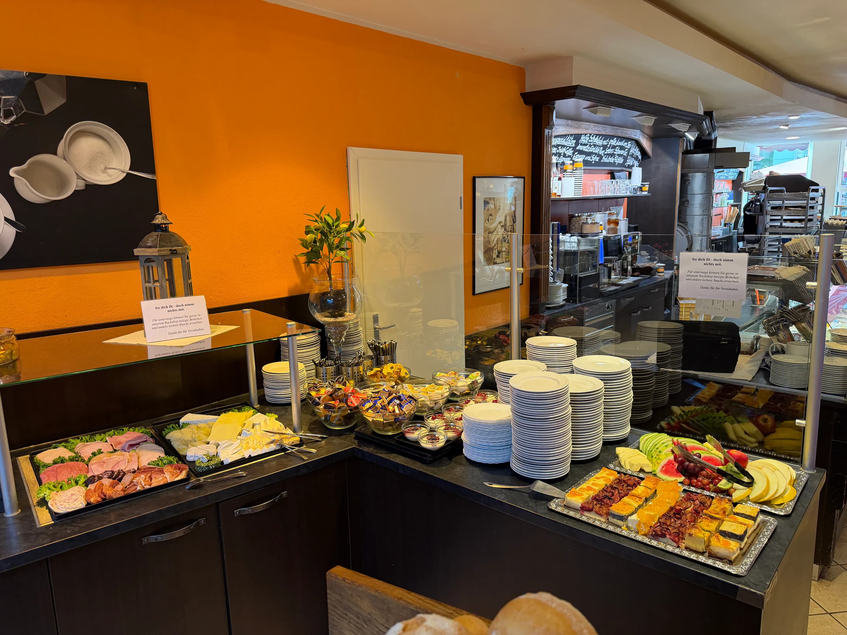 Vollständig angerichtetes Frühstücksbuffet mit Aufschnitt, Käse, Obst, Joghurt und kleinen Kuchenstücken
