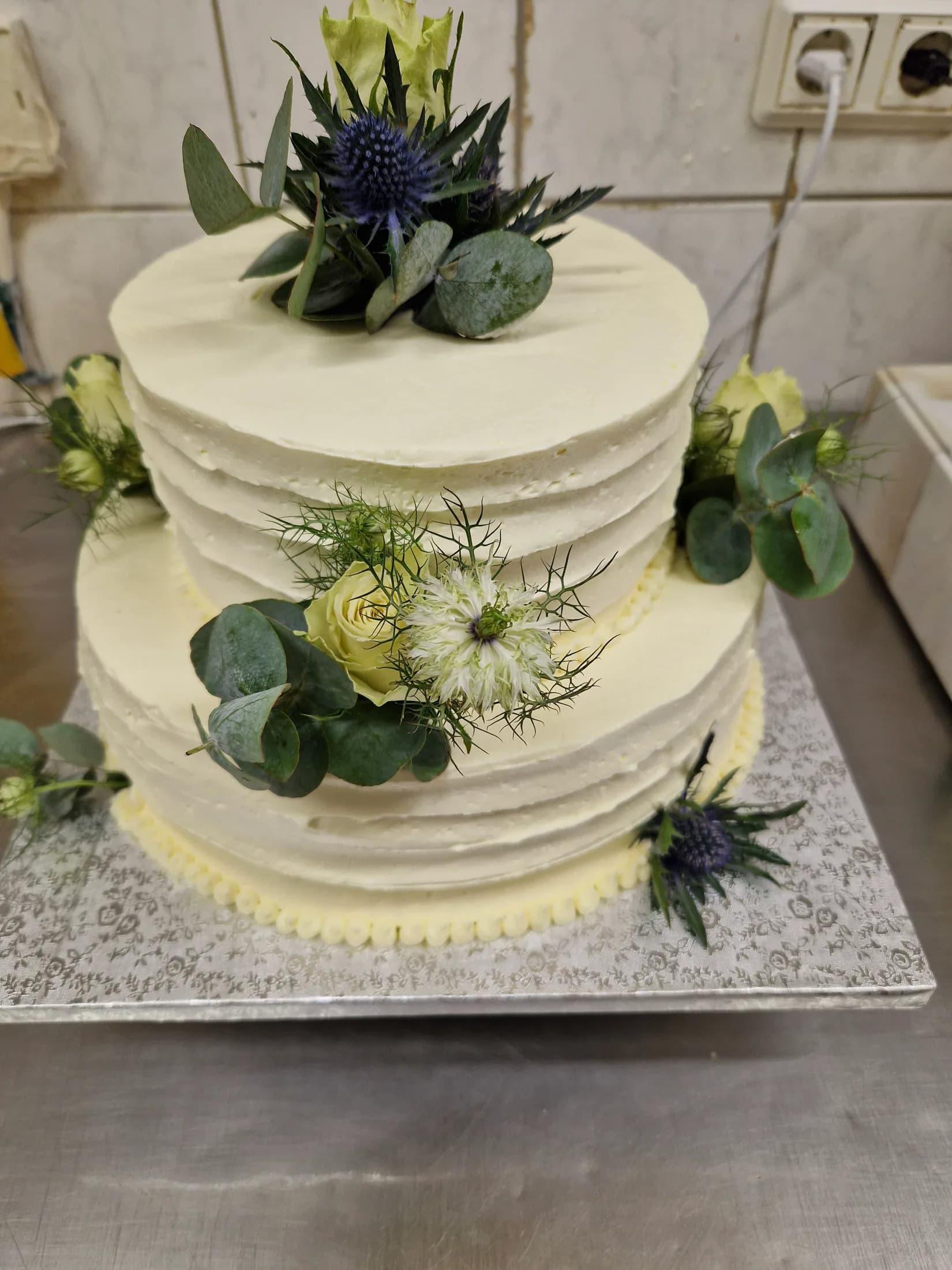 Zweistöckige Hochzeitstorte mit weißen Blüten, Disteln und Eukalyptus